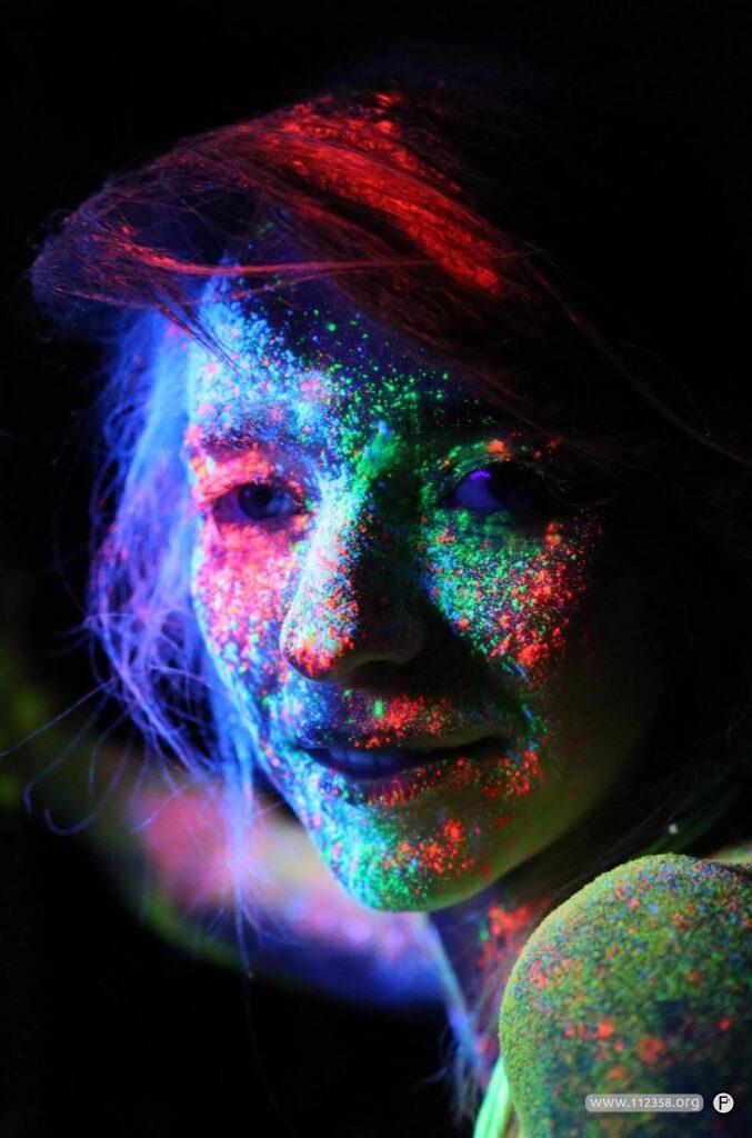 Twarz oświetlona farbami fluorescencyjnymi w świetle lampy UV, w odcieniach czerwieni, zieleni i błękitu